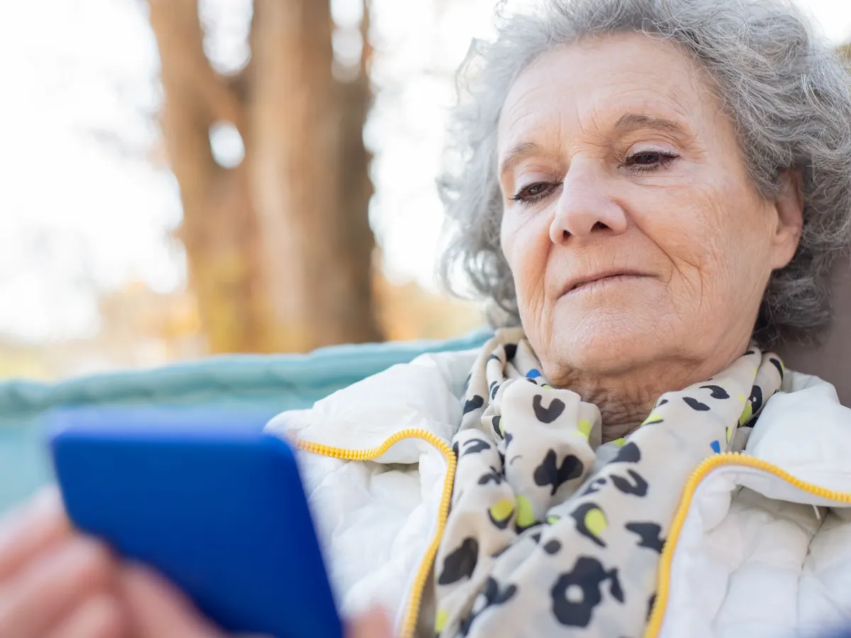 Older woman with gray hair reading her phone outdoors.