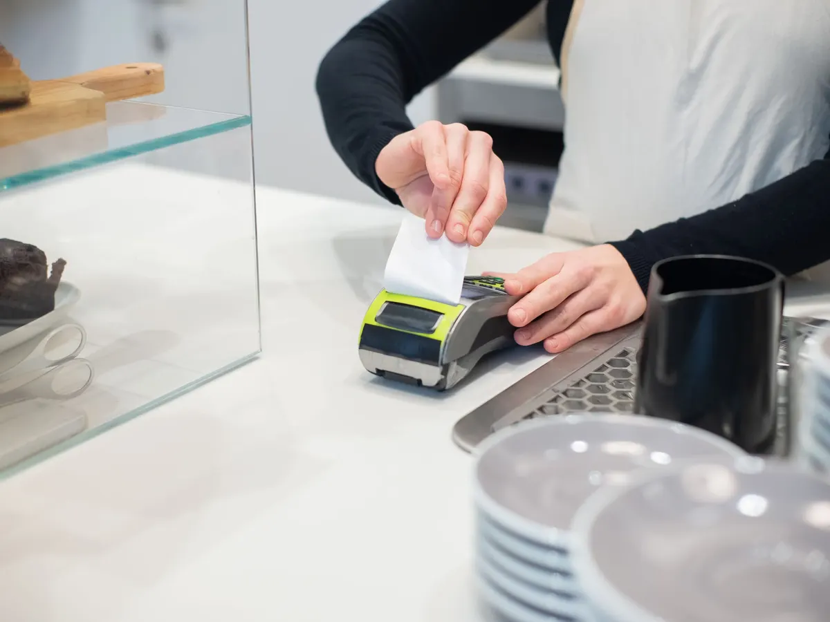 Cafe worker tearing a receipt from a card terminal on a white counter.