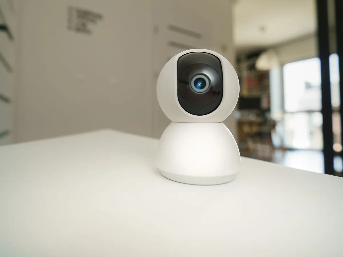 White home security camera on a table in a bright living room.