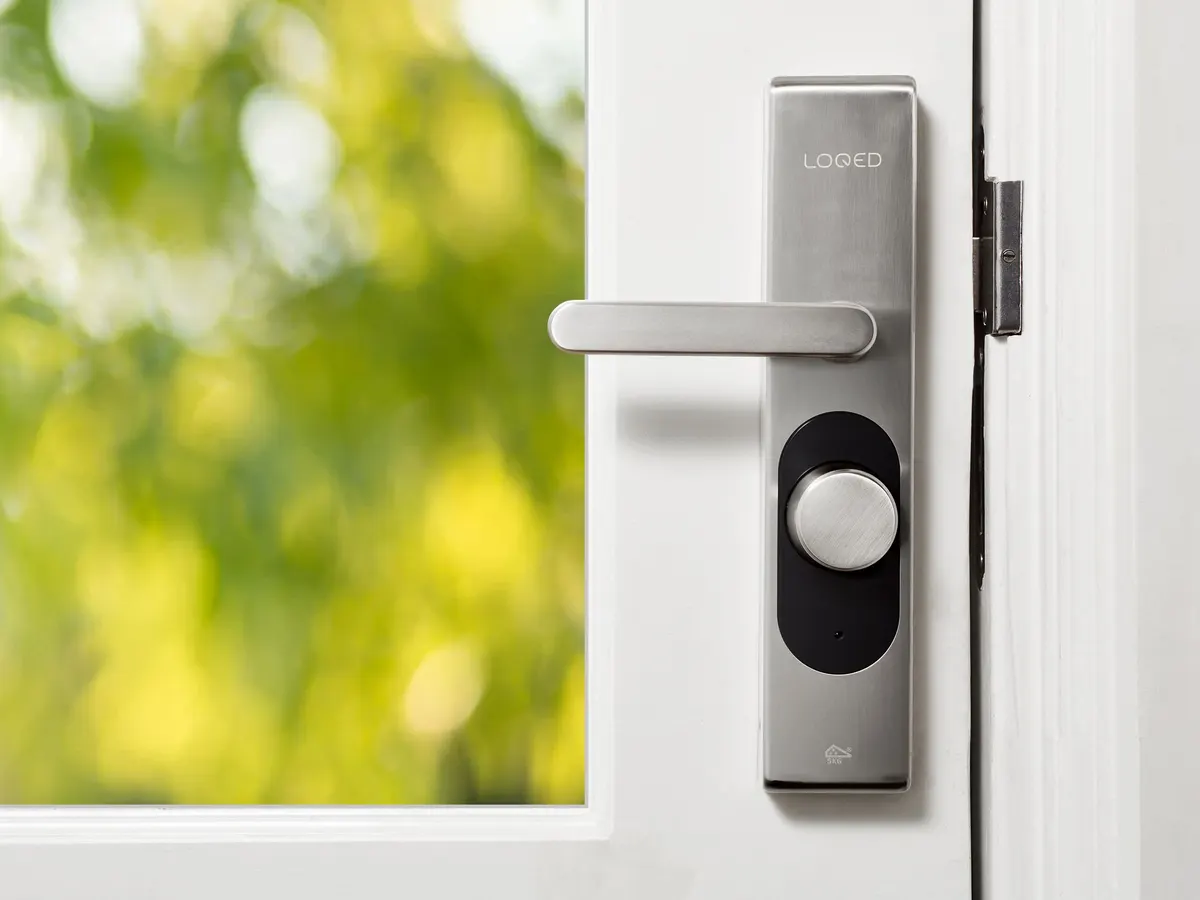 Smart lock with a lever handle on a white door, green garden behind the glass.