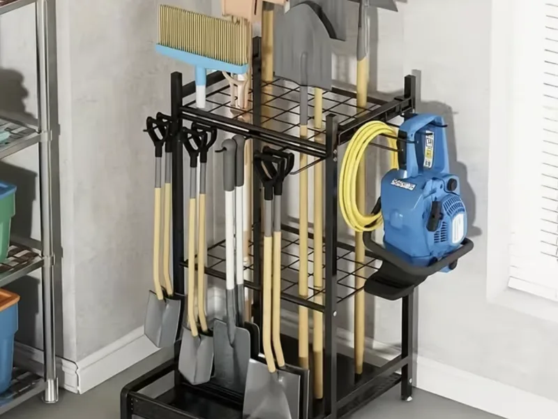Metal garden tool rack holding rakes, shovels and a hose.